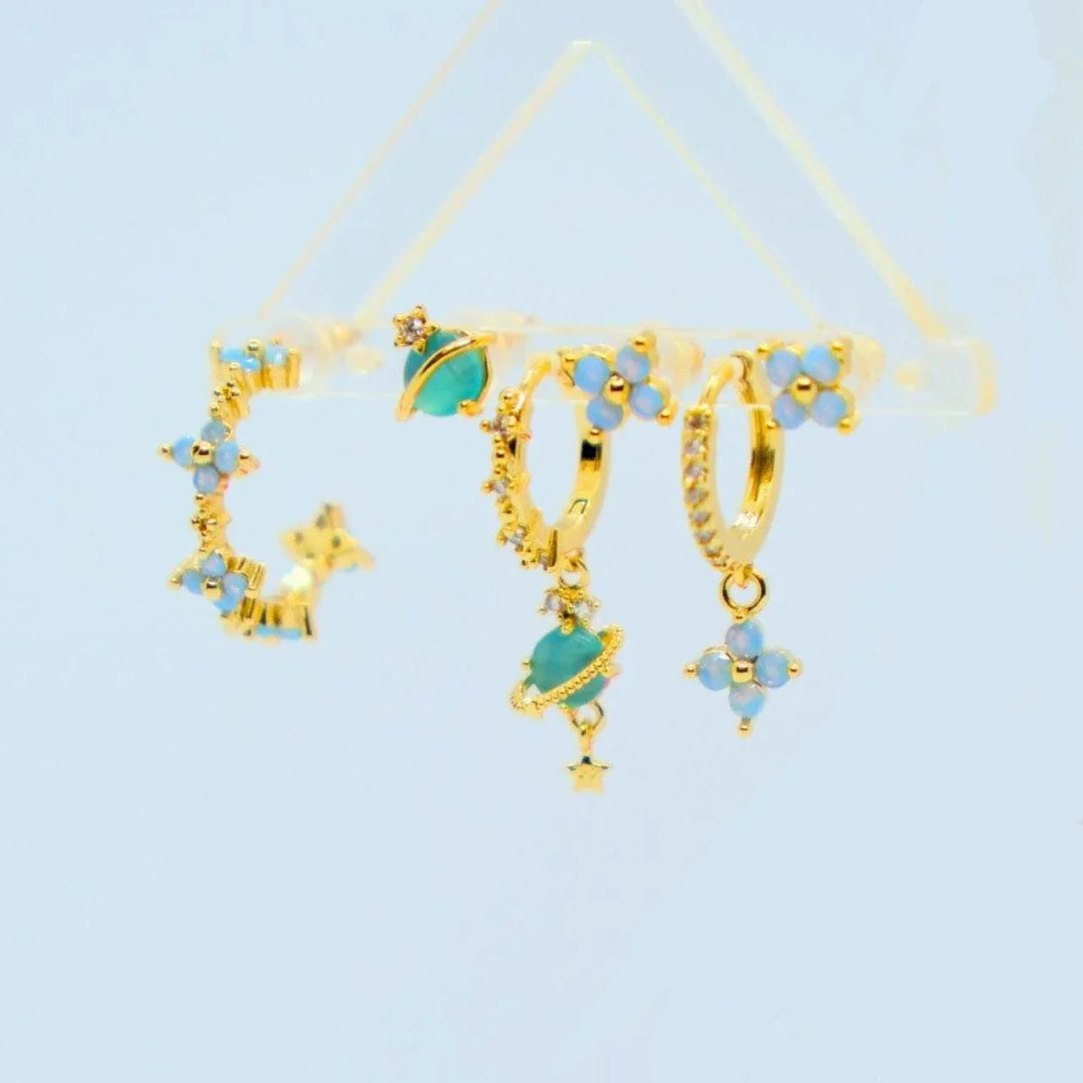 Gold-tone stacking earrings with blue flower charms, teal moons, and star accents