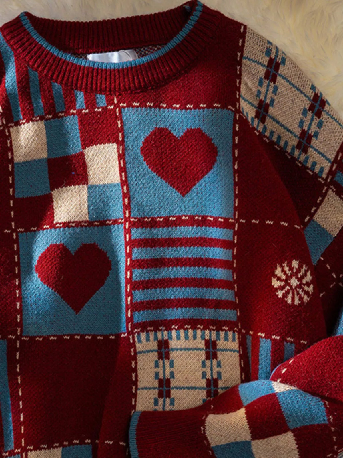 Men's patchwork sweater front detail with red hearts, beige plaid, and teal striped blocks