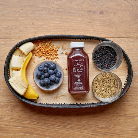 Organic botanical beverage bottle with sliced fruit and dried herb bowls on tray
