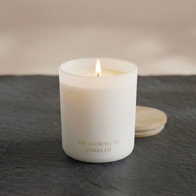 White pillar candle in frosted jar, lit wick, The Roosevelts Candle Co label