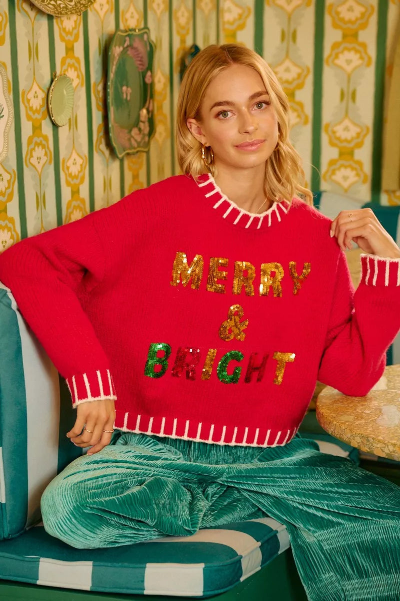 Red knit holiday sweater with sequined “MERRY BRIGHT” across the chest and hem