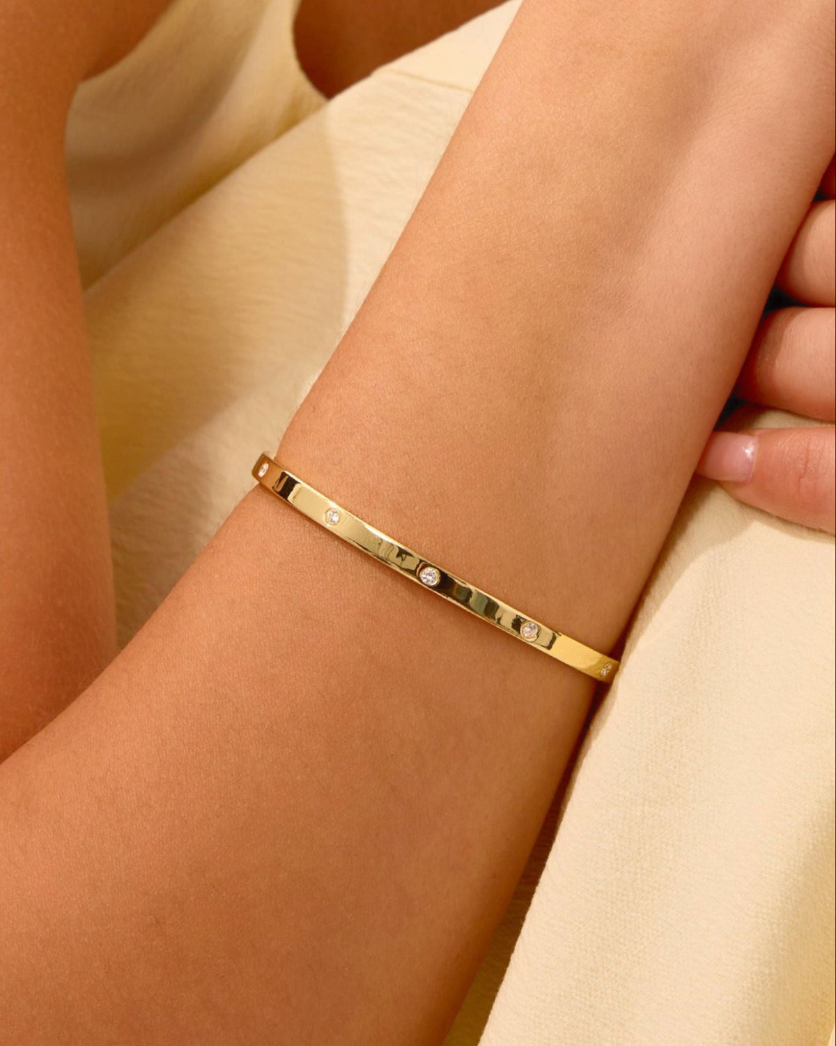 Slim gold bangle with small round diamond stones along the center bar, on wrist
