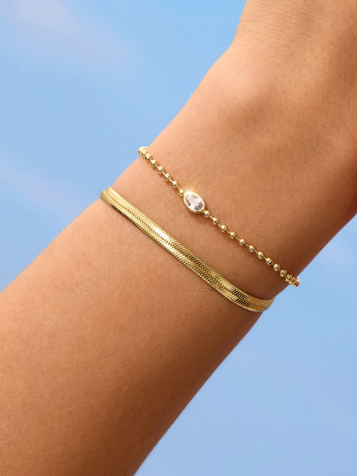 Gold-tone bracelet with oval stone charm and beaded chain detail on wrist