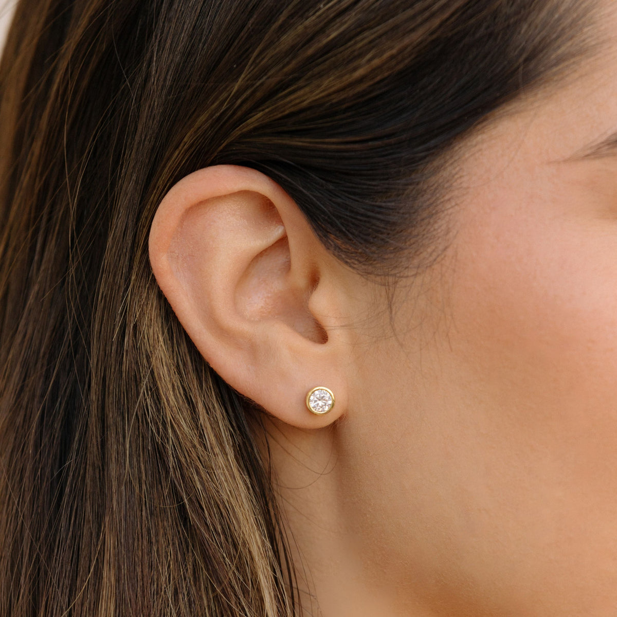 Gold round diamond bezel stud earrings, side view on ear