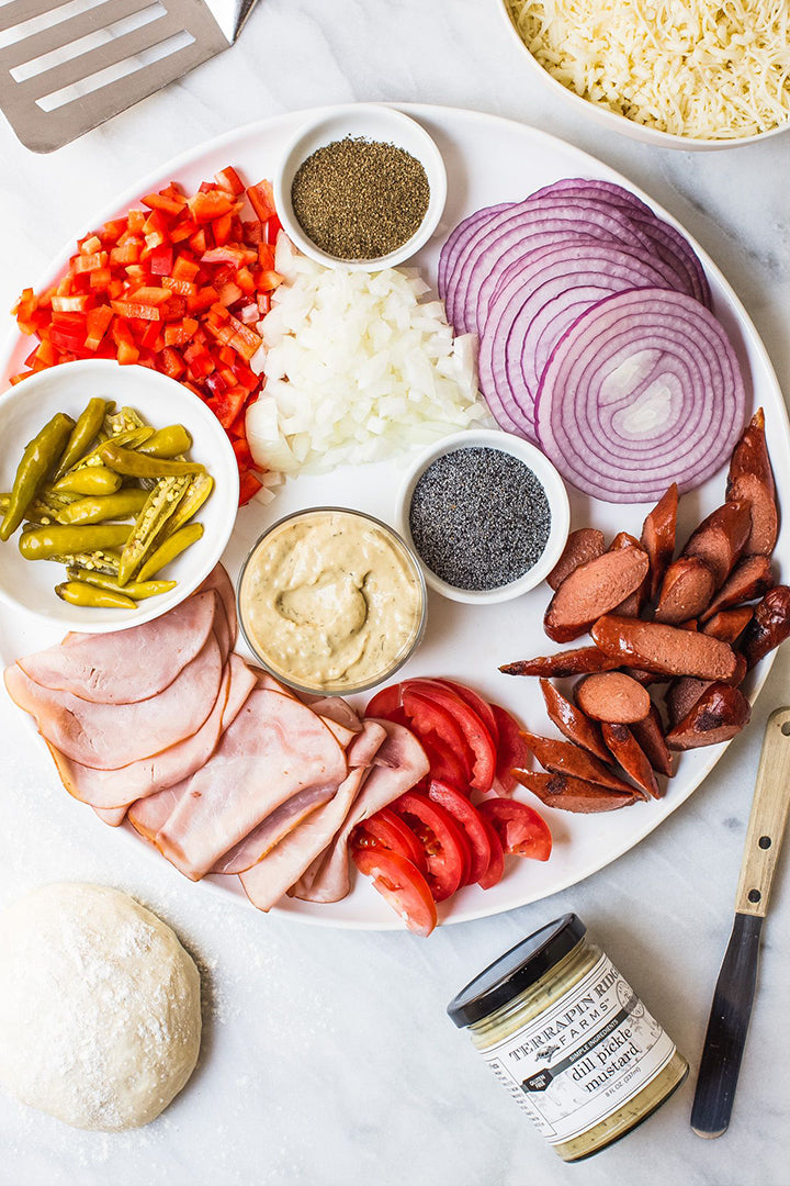 Small jar of dill pickle mustard on platter with chopped vegetables and pickles