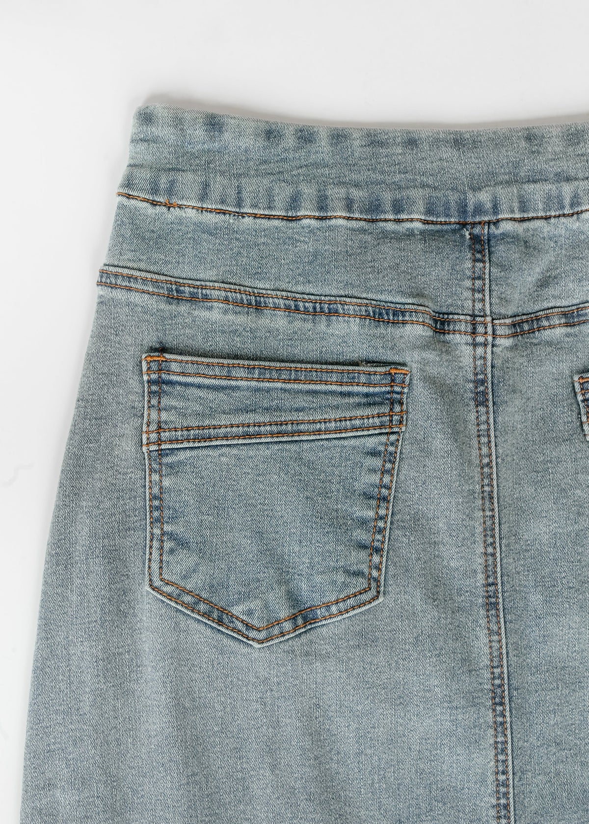 Light wash denim skirt pocket close-up with contrast orange topstitching