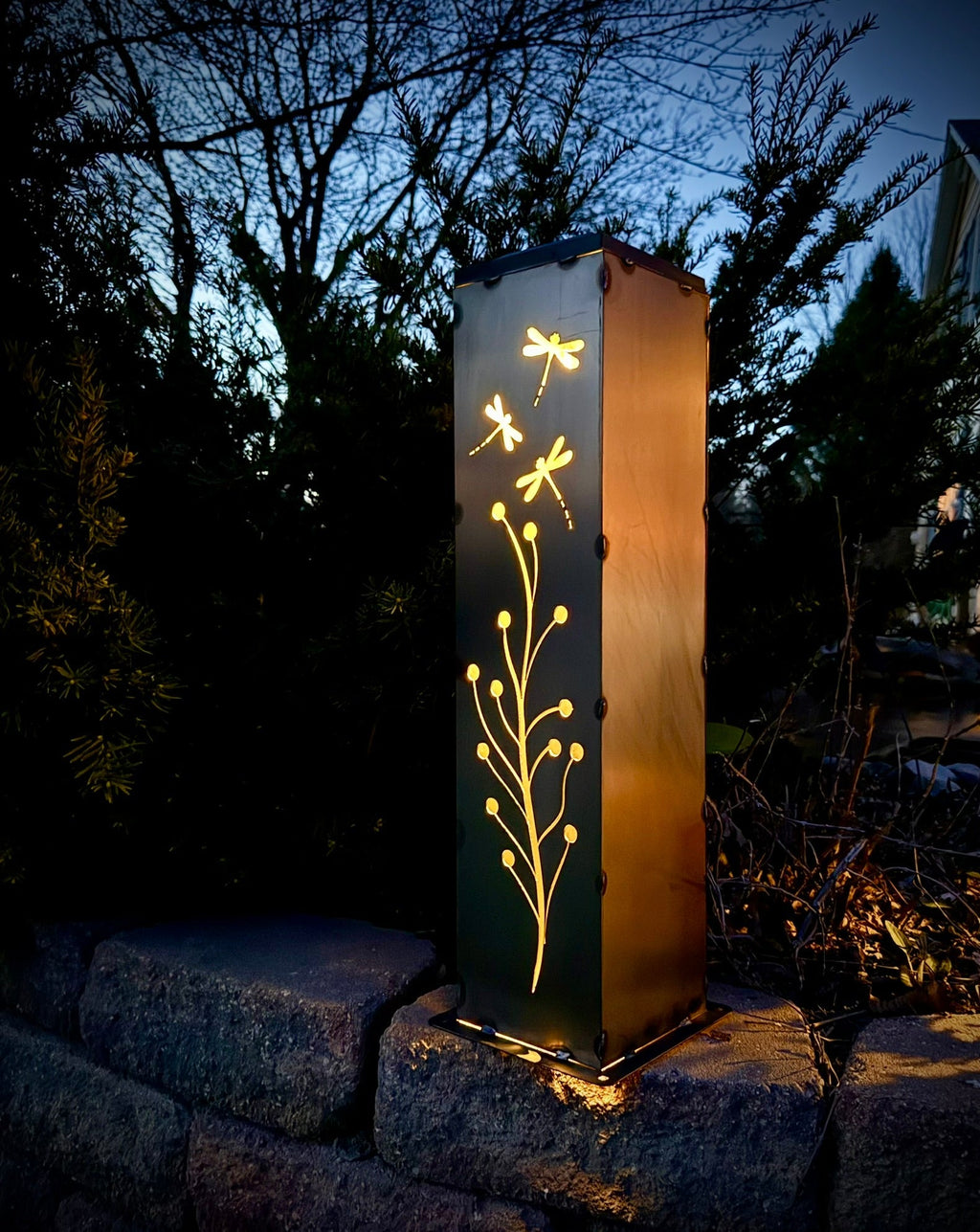 Steel solar luminary pillar glowing with golden dragonfly and branch light pattern