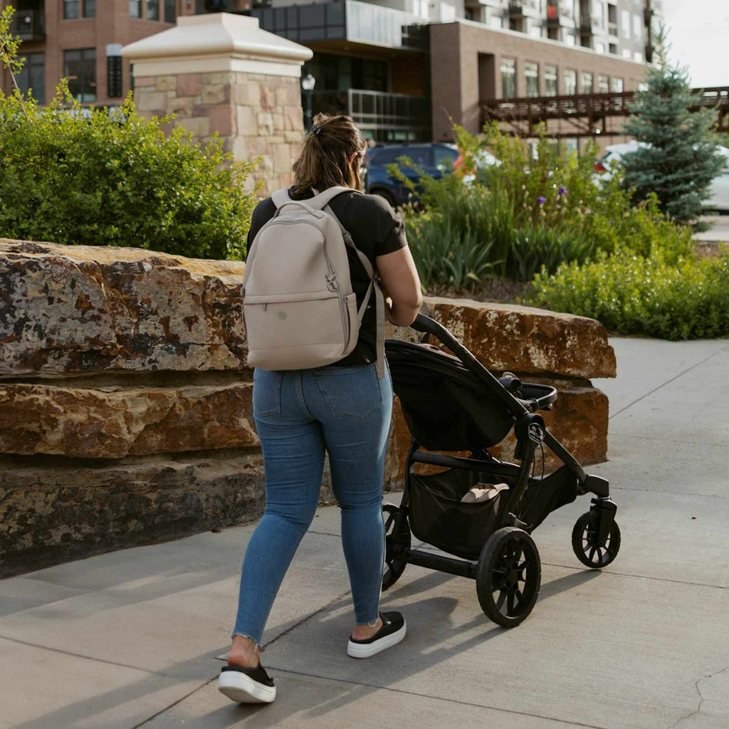 Beige diaper backpack worn by parent, with front organizer pocket and top handle