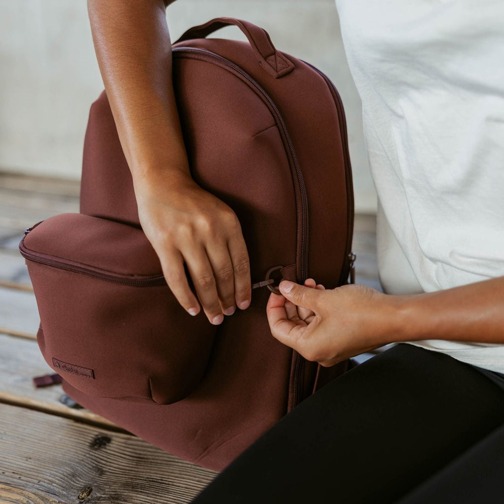 Maroon diaper backpack open with hands adjusting the top zipper area