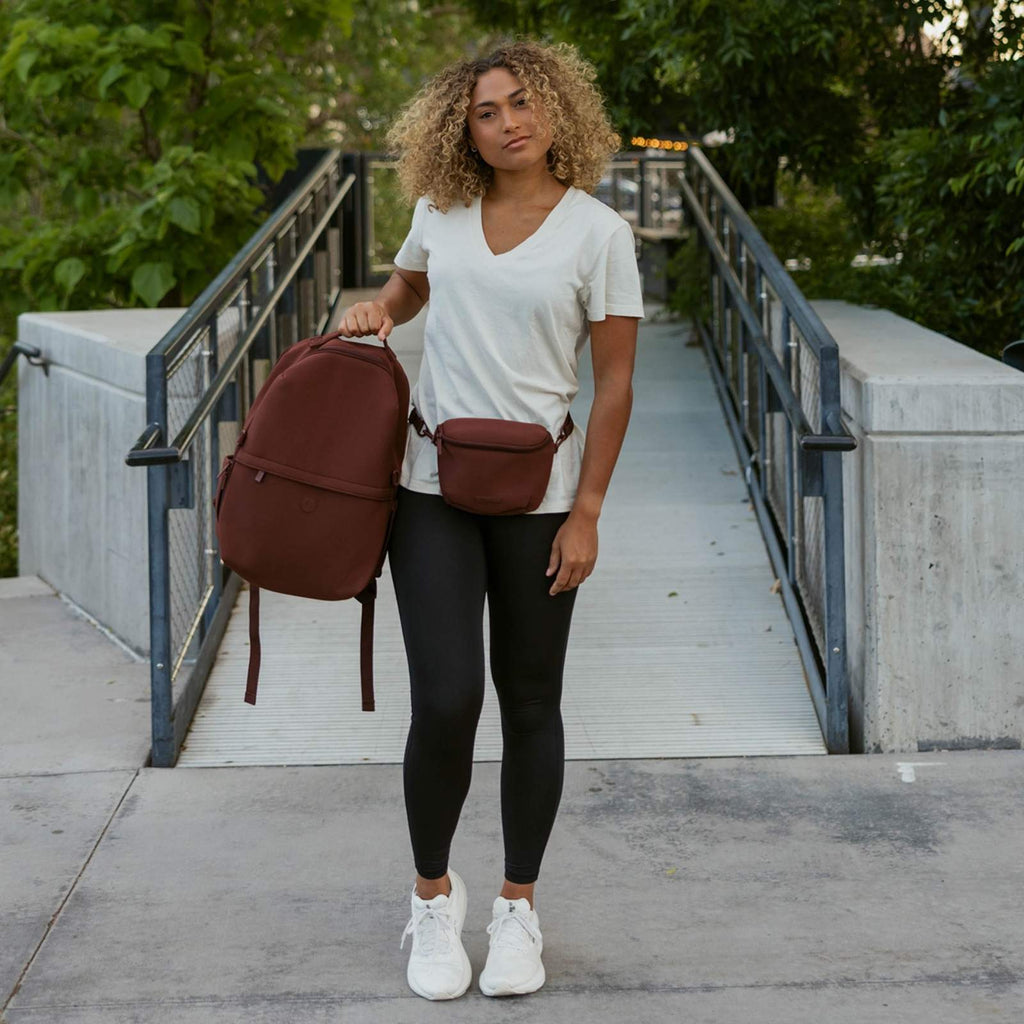 Maroon neoprene diaper backpack worn crossbody with adjustable shoulder strap