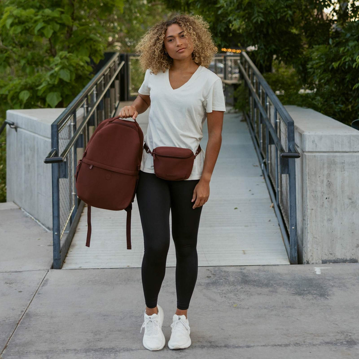 Maroon neoprene diaper backpack worn crossbody with adjustable shoulder strap