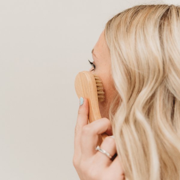 Facial dry brush with wooden handle and soft bristles, used on cheek