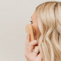 Facial dry brush with wooden handle and soft bristles, used on cheek