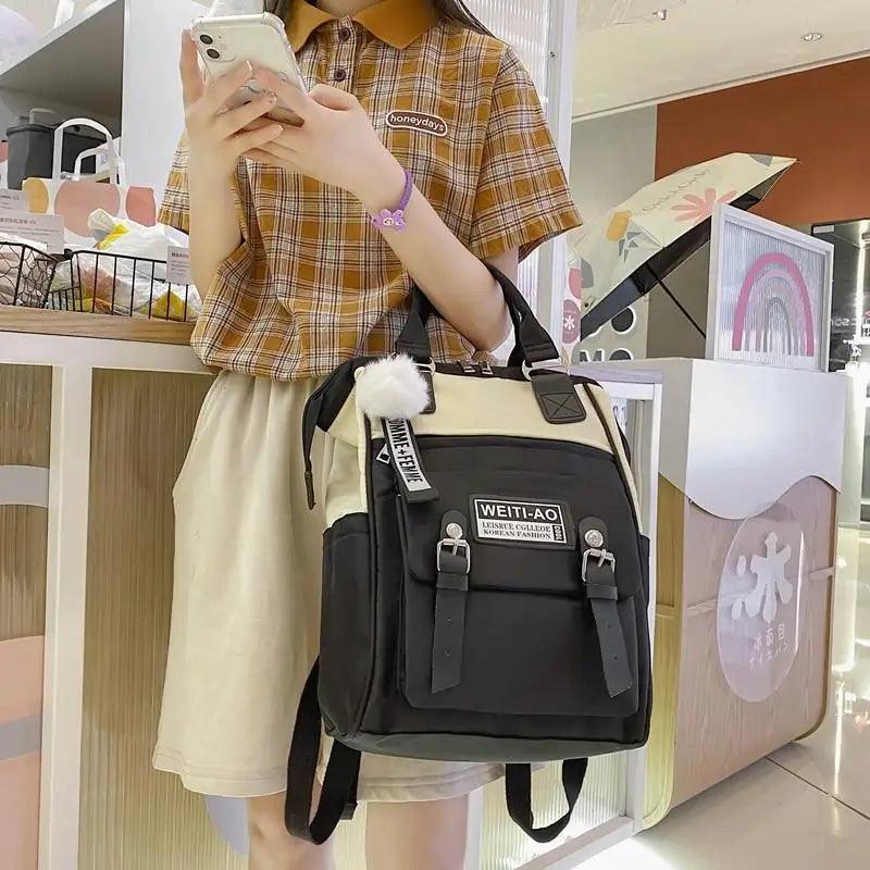 Black and cream backpack with front pocket, pom-pom key charm, and shoulder straps