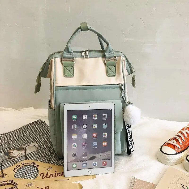 Light green backpack with tablet sleeve front panel and small pom-pom charm