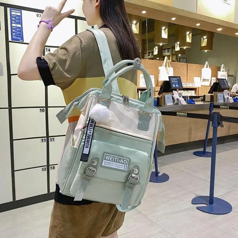 Light green backpack with front label panel, pom-pom charm, and top handles