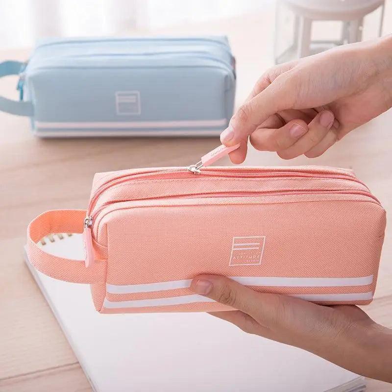 Pink double-layer pencil case with white stripe and zippered front, held by hand