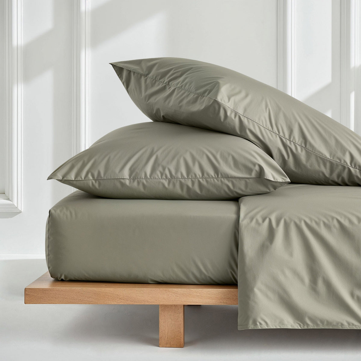 Olive green pillowcase set with two pillowcases on a bed with draped fabric