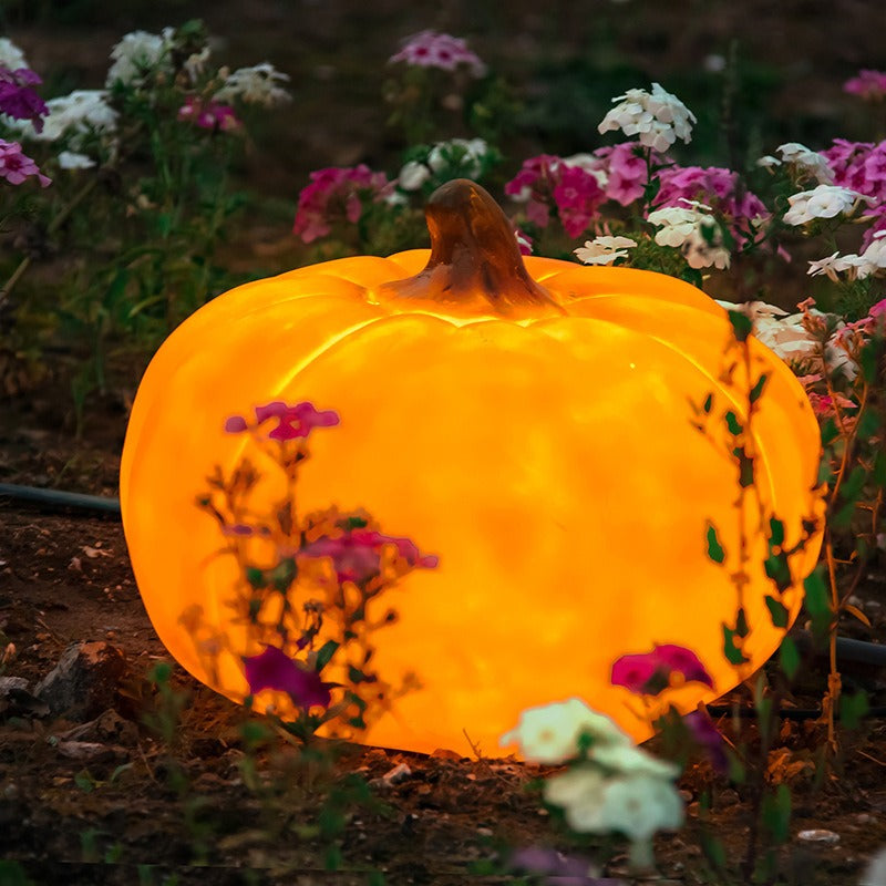 Close-up glowing golden yellow pumpkin-shaped LED outdoor light in garden soil