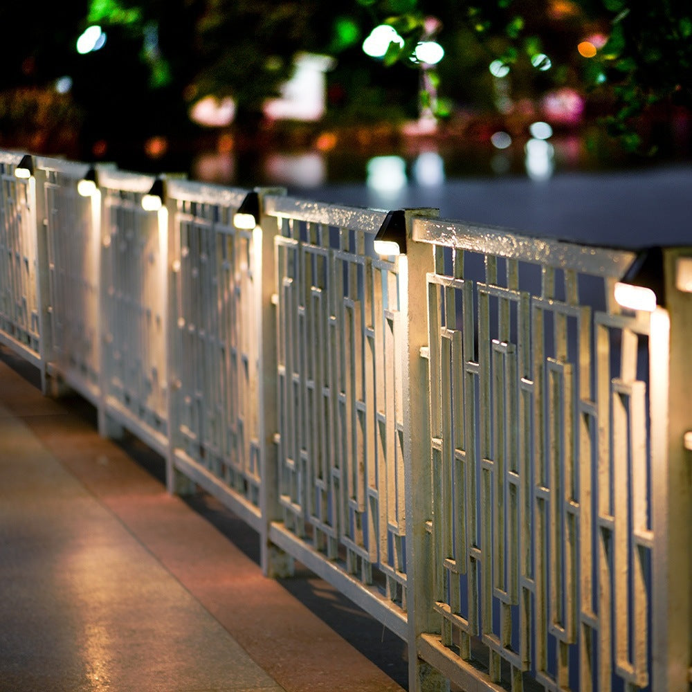 Solar LED path lamps along a fence railing, emitting warm light from square heads