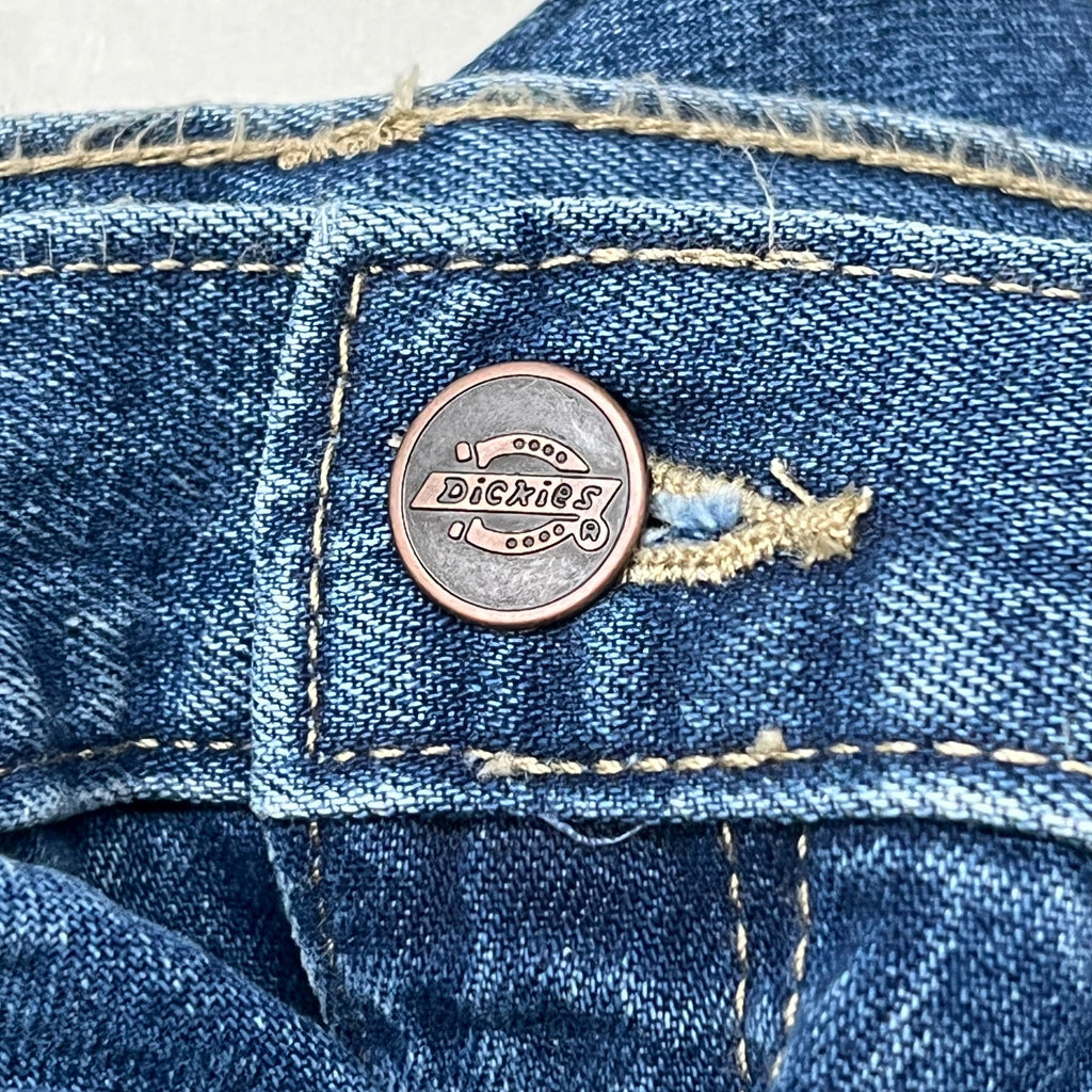Riveted leather-look logo button on blue denim waistband of carpenter jeans.
