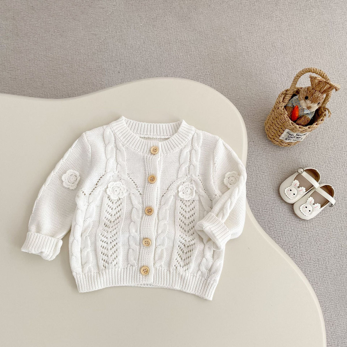 Cream baby knit cardigan with cable-knit texture, floral appliques, gold button closure