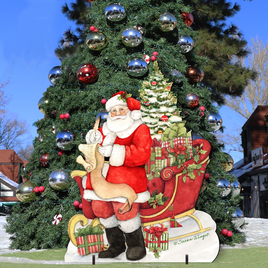 Christmas Santa yard sign leaning on base with tree and wrapped gifts in red and green