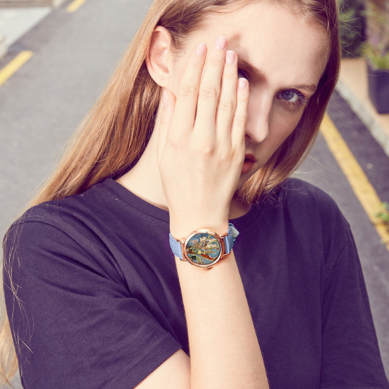 Quartz wristwatch on wrist with blue strap and rose-gold case, round colorful art dial