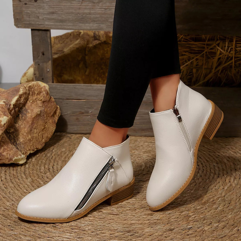 White block-heel ankle boots with side zipper and tan sole, worn with black pants