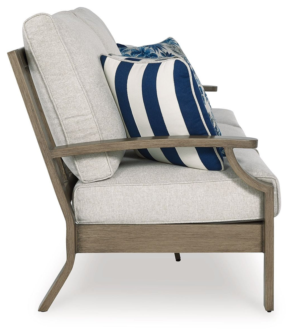 Outdoor sofa arm section with light gray cushion and blue striped floral pillow