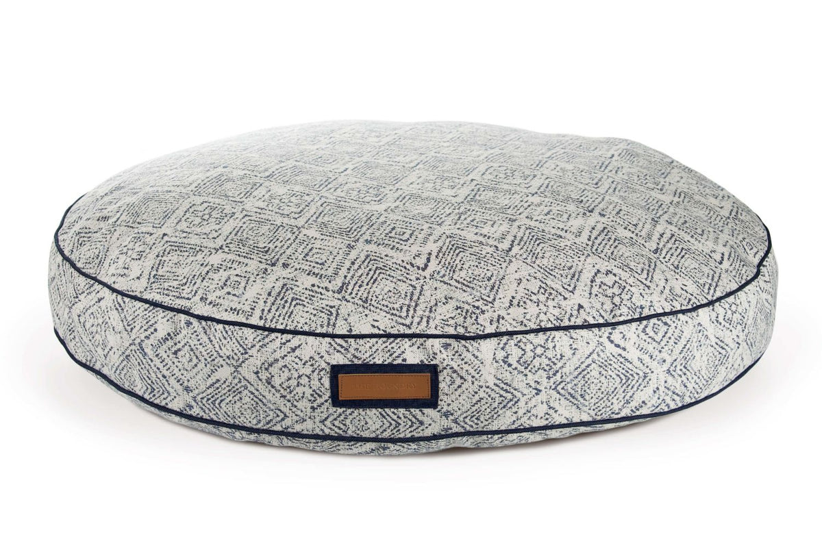 Round pet bed with gray geometric top and dark blue piping; front label tab