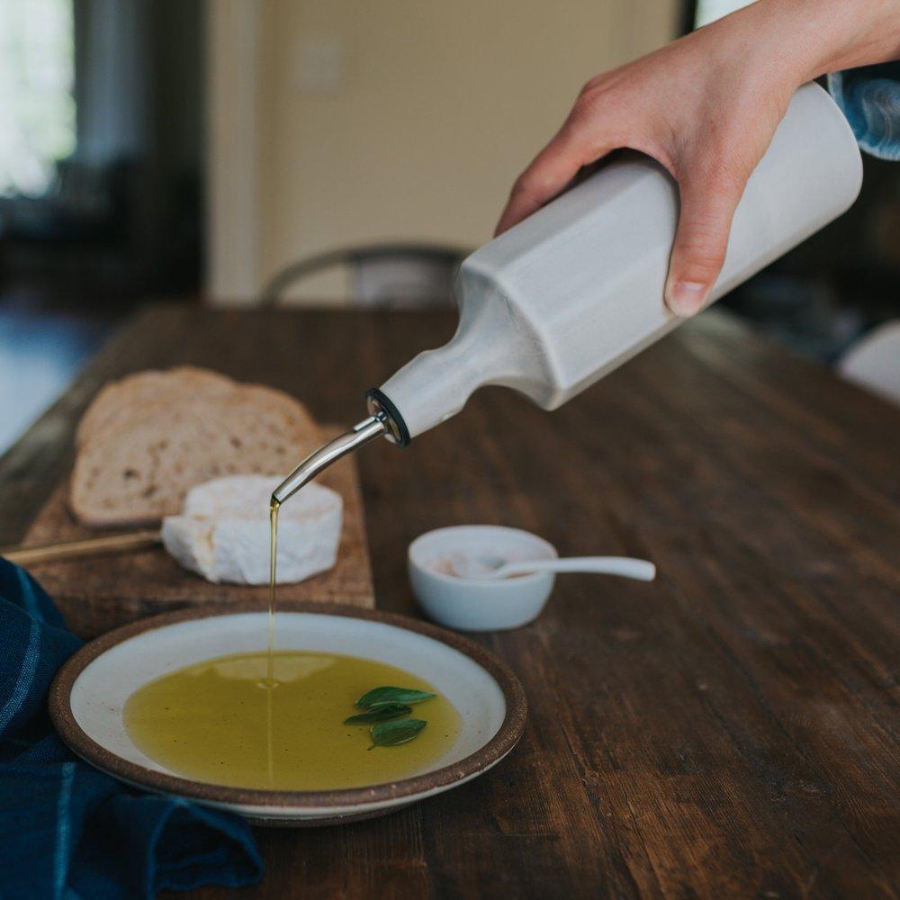 Silk white porcelain olive oil dispenser pouring oil onto serving dish