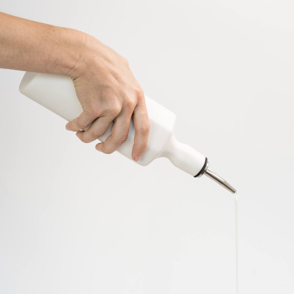 Silk white porcelain olive oil dispenser held in hand, pouring stream