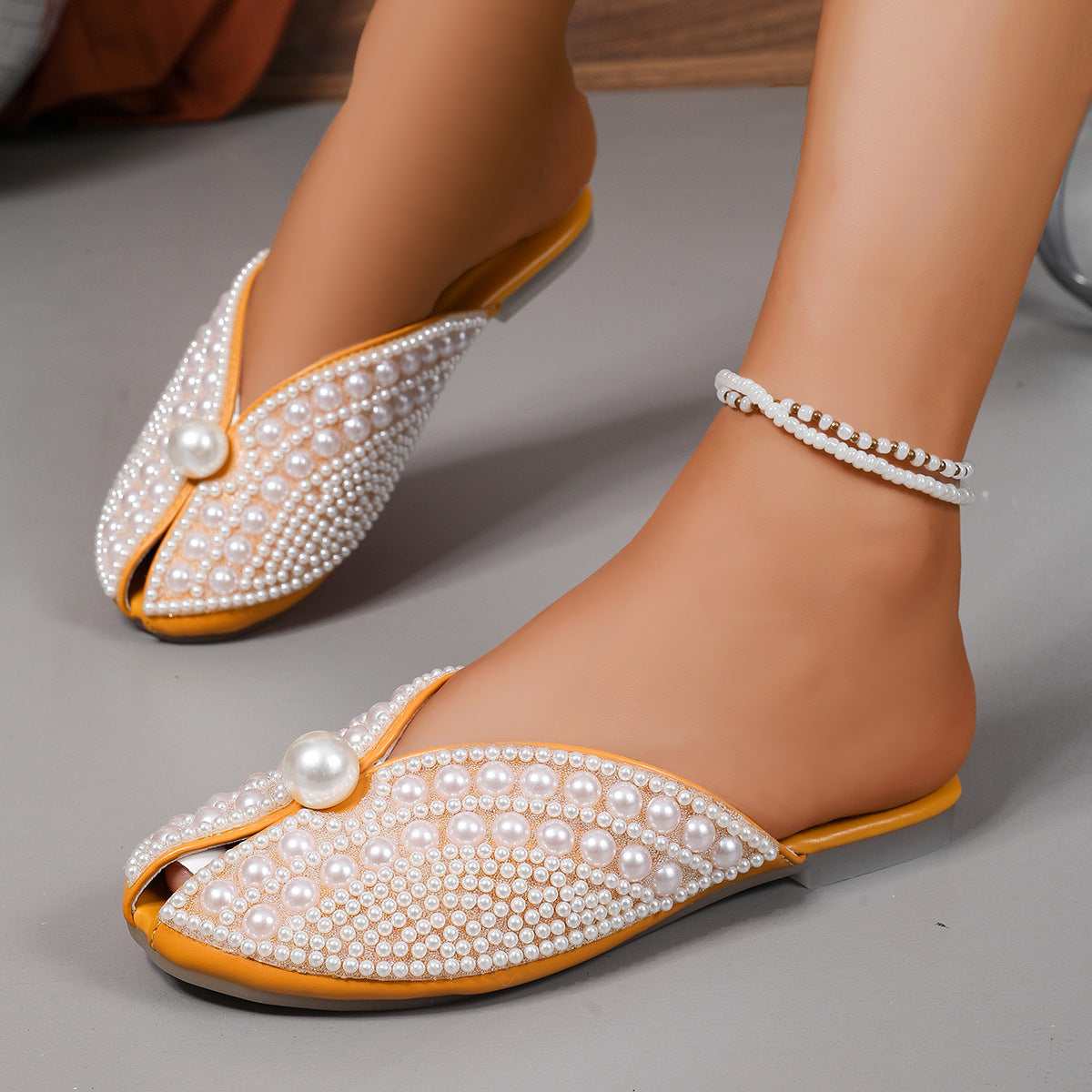 Pearl-embellished covered-toe flat slippers with bow detail and yellow outsole on feet