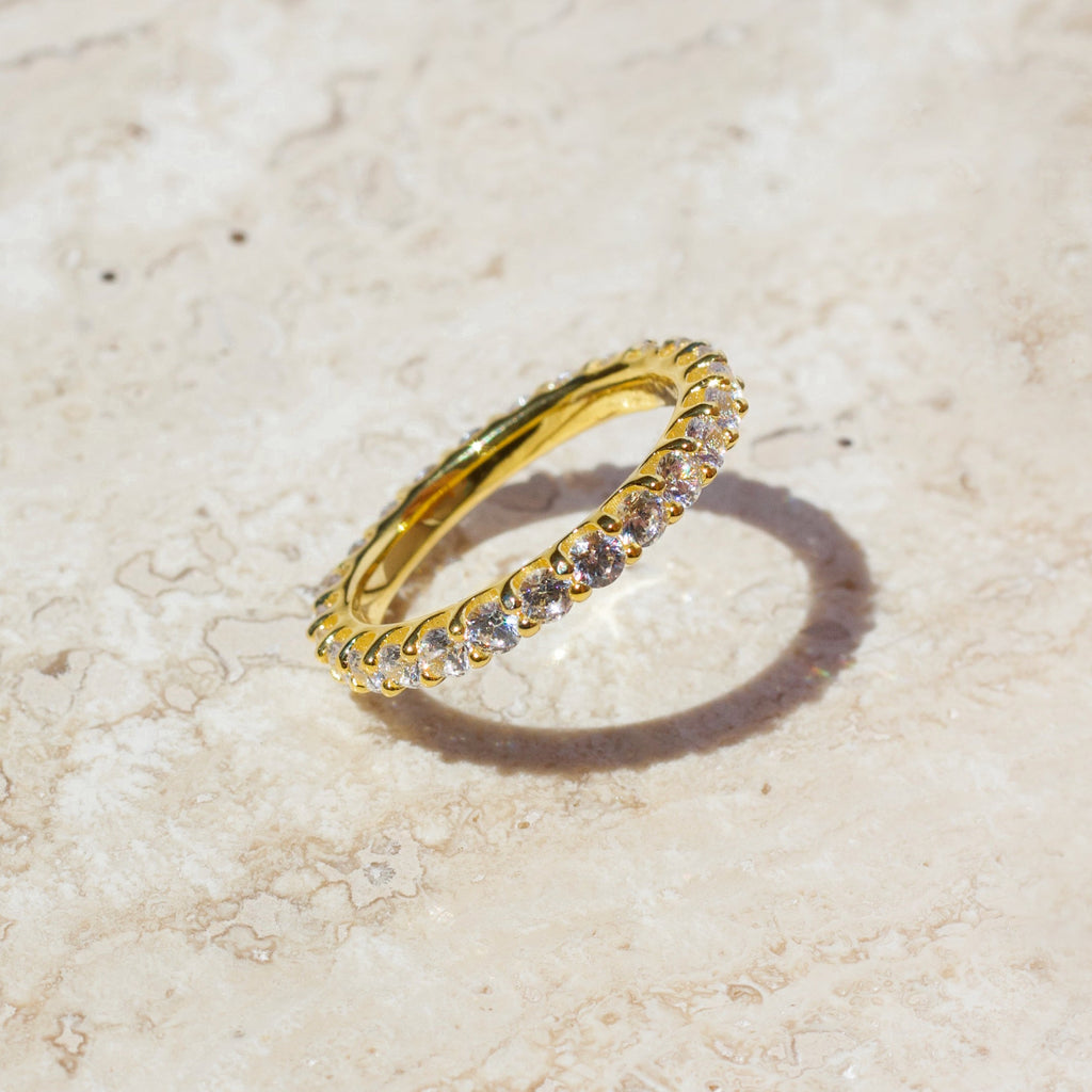 Gold eternity ring with clear stones, angled close-up on light surface