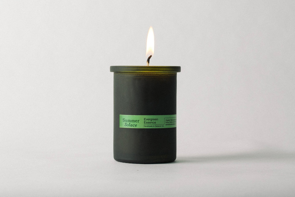 Lit dark green candle in a glass jar with cork lid and green label