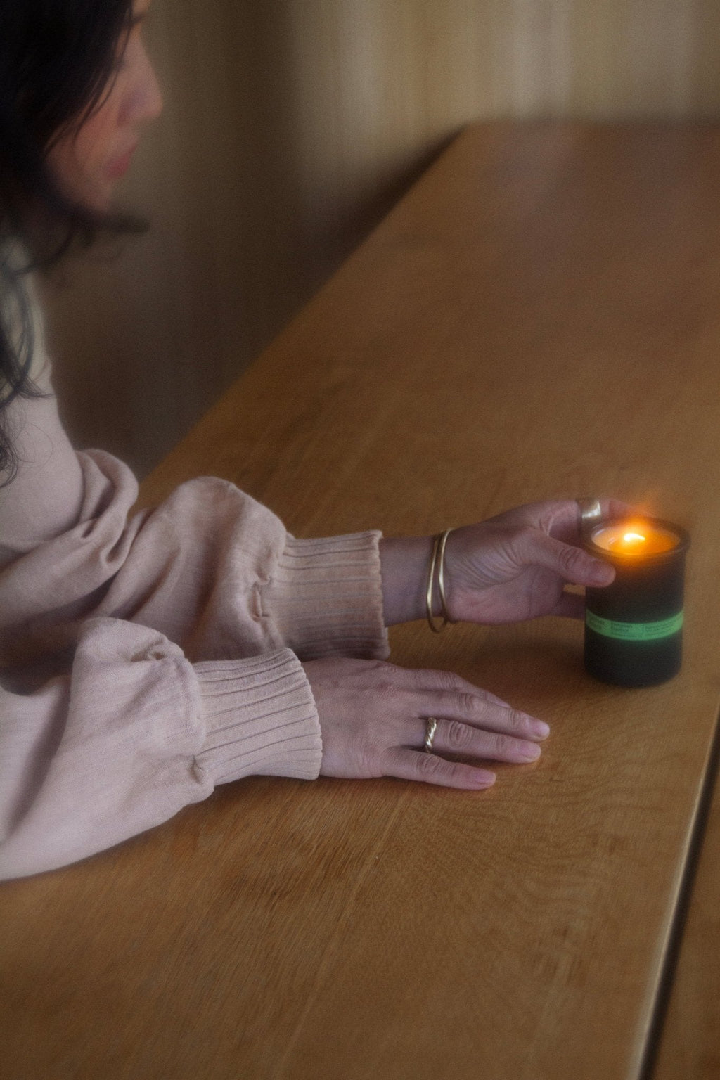 Lit dark green candle jar held by hand on a wooden tabletop