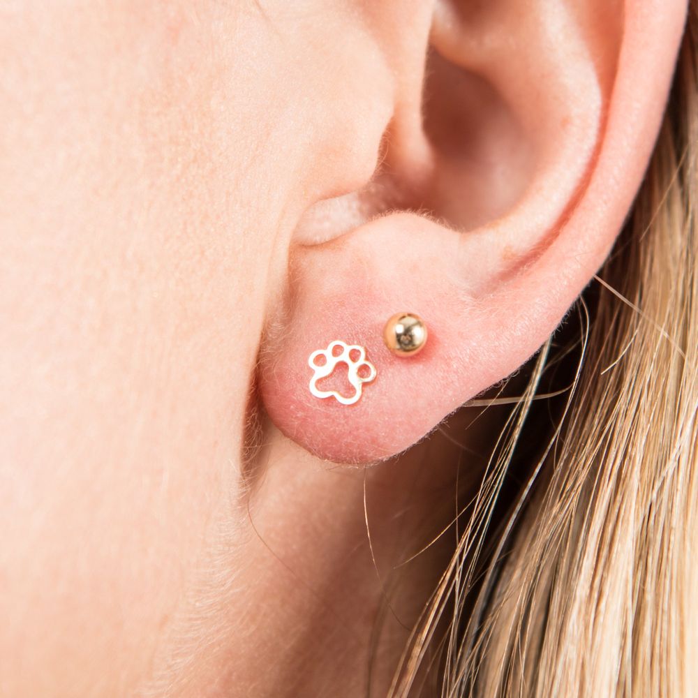 Dog paw stud earring on ear, gold-tone paw charm stud