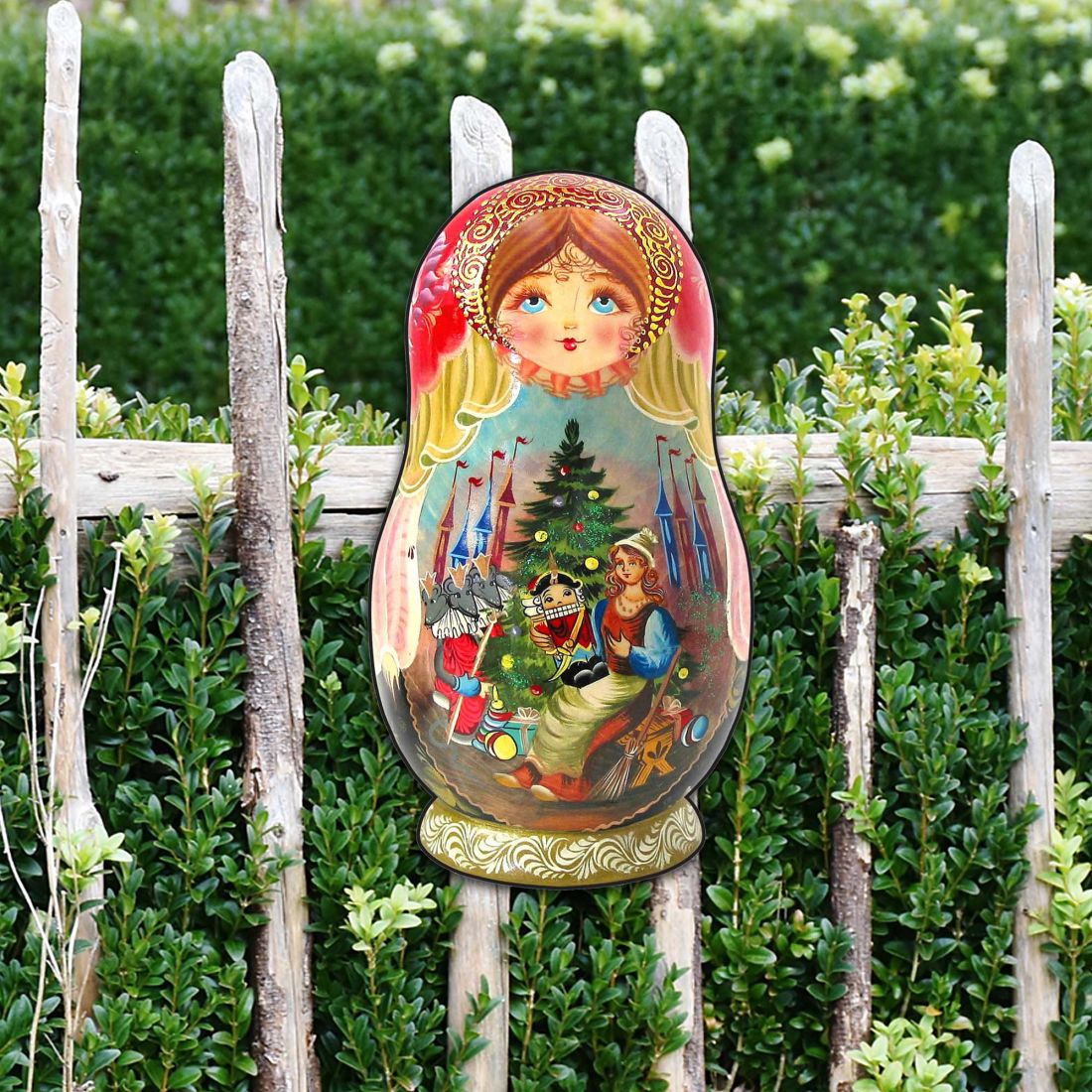 Outdoor large nesting doll ornament in front of green shrubs on white stakes