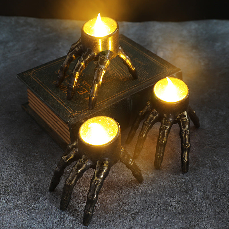 Skeleton hand lantern candle holder with three lit candles on a base