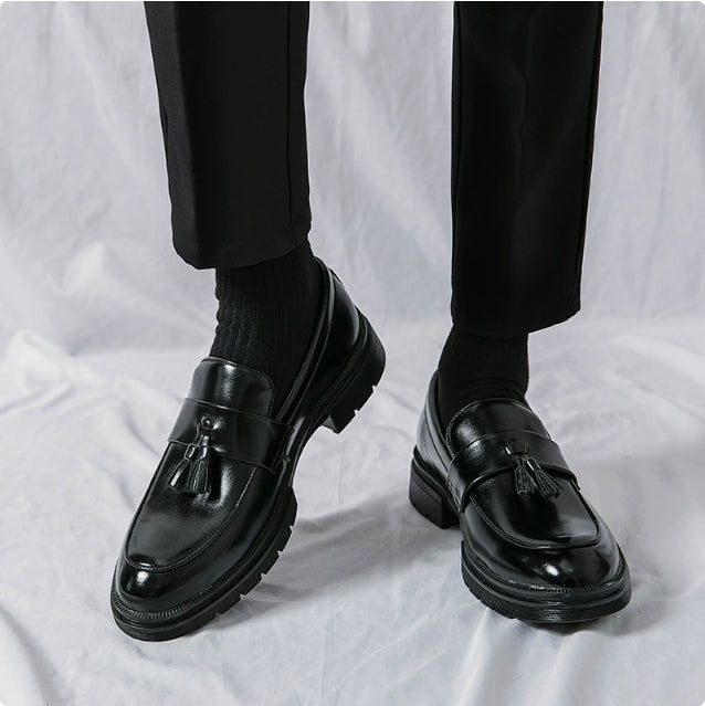 Black leather tassel loafers with glossy finish and chunky rubber sole