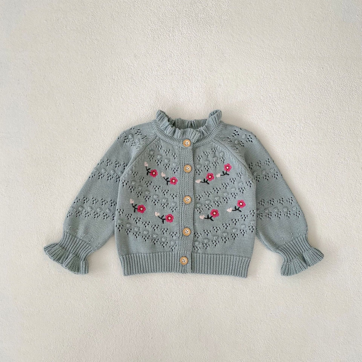 Blue-gray knitted cardigan with red floral embroidery and button front, ribbed hem.
