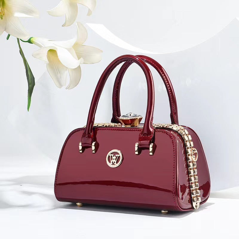 Wine red patent leather handbag with top handles, chain strap, and diamond clasp