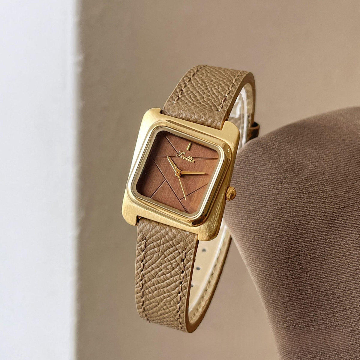 Square quartz watch with gold case, tan leather strap, and brown dial