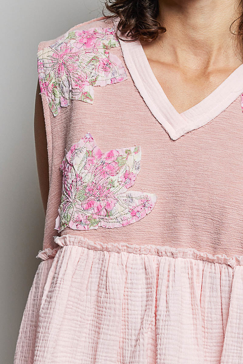 Close-up of pink sleeveless top with white V-neck trim, floral patch applique, raw edges