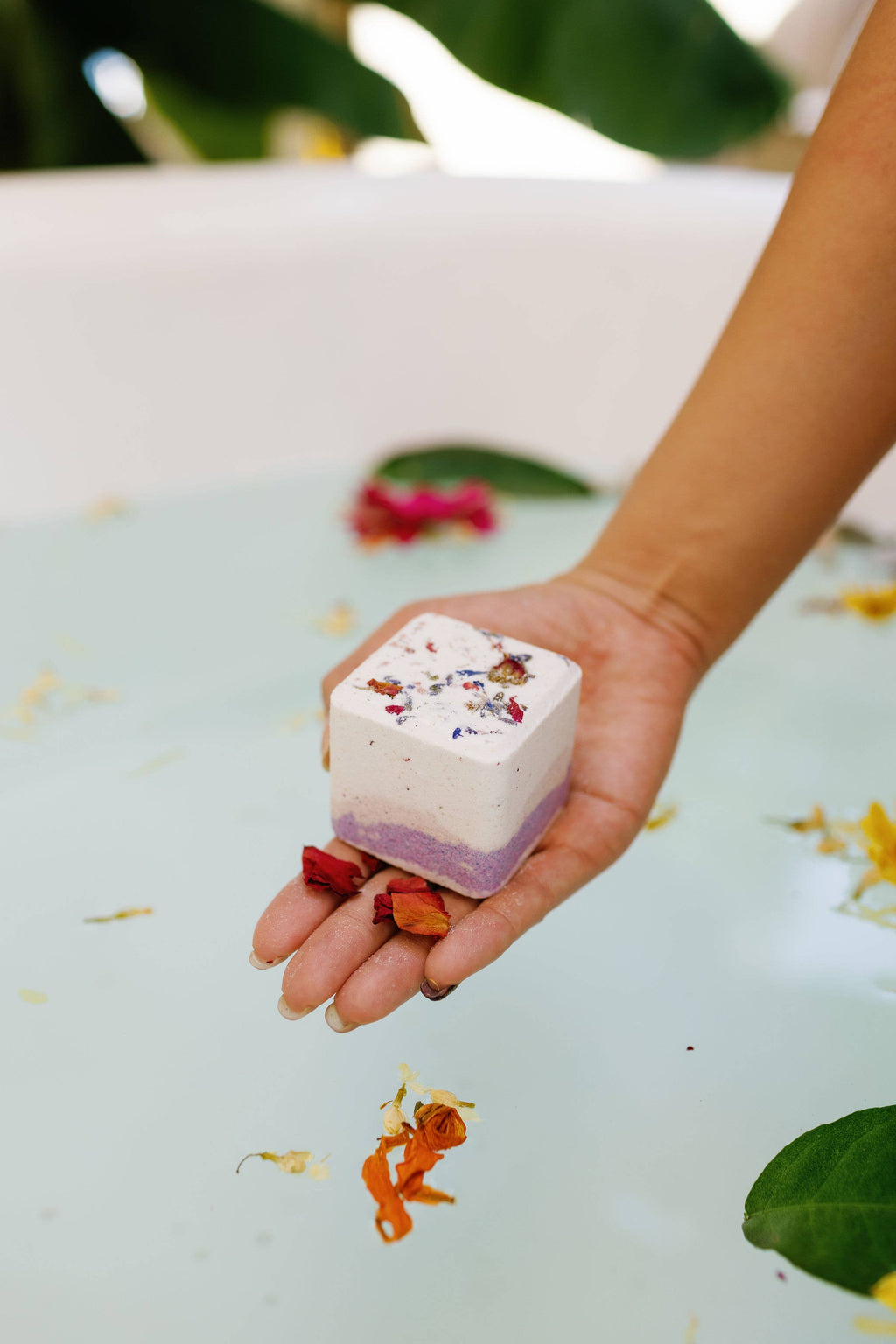 Square bath bomb with lavender gradient and colorful flower sprinkles, held in a hand