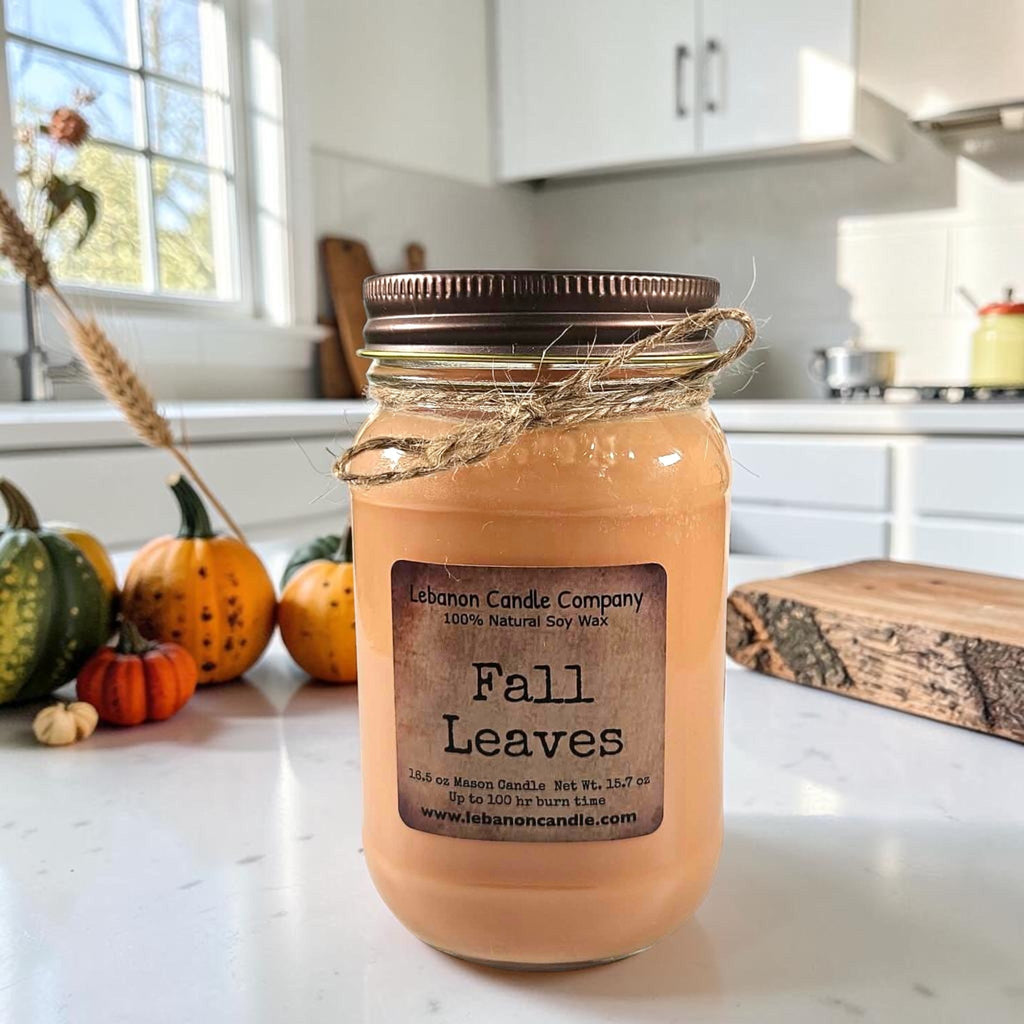 Amber jar candle with twine bow, dark lid, and centered “Fall Leaves” label