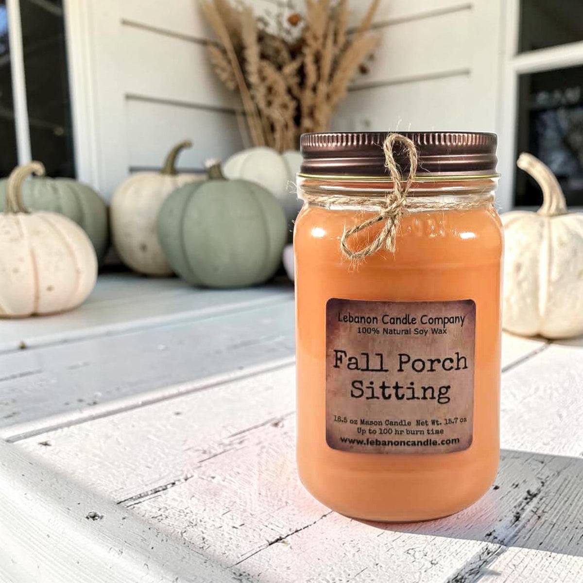 Fall Porch Sitting soy wax candle in amber glass jar beside seasonal pumpkins