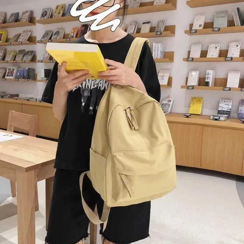 Beige backpack with drawstring cords and front pocket, worn while carrying books