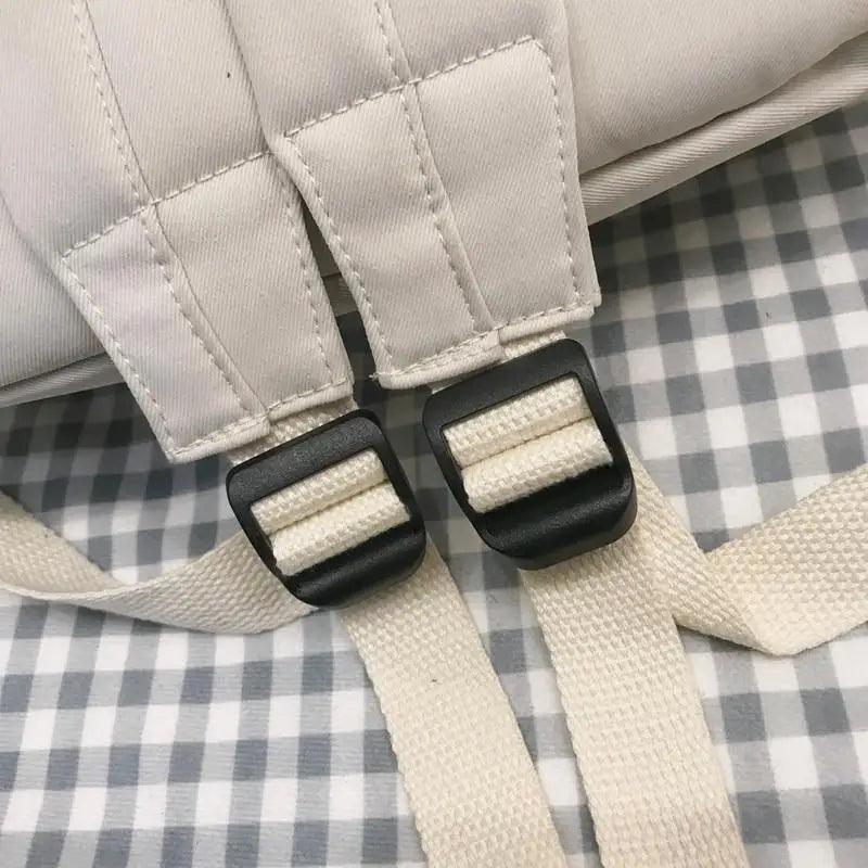 Cream backpack with black plastic buckle and woven adjustable strap